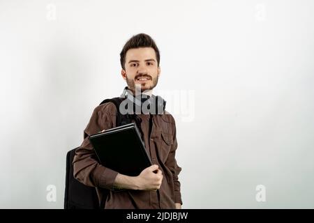 Young man smiling confident wearing casual clothes posing isolated over white background student with books and backpack and looking at the camera. Hi Stock Photo