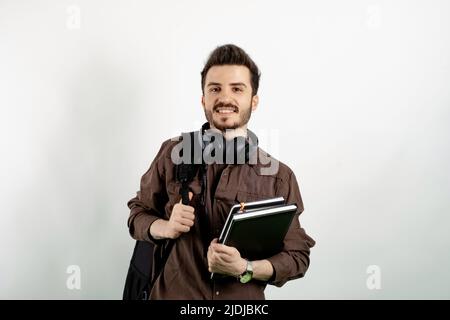 Cheerful caucasian man wearing brown shirt posing isolated over white background student with books and backpack and looking at the camera. High schoo Stock Photo