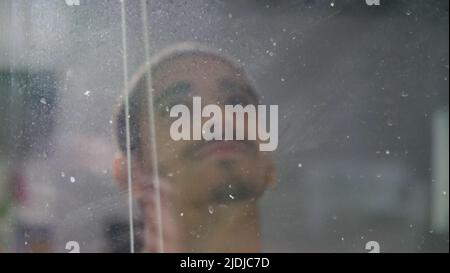 Young arabic man looking at the sky through dirty window. Smiling Male closeup view. Stock Photo