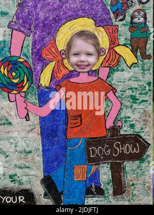 Young child at head in hole photo board at a fair, Cornwall, UK Stock Photo