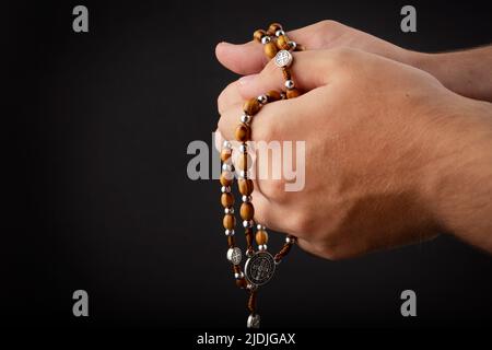 Folded hands of a young man holding a rosary during a pray isolated on black background Stock Photo