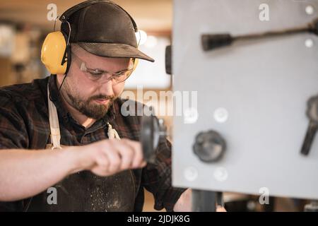 Closeup serious and concentrated man worker, carpenter in protective coverall, glasses, headphones work with grinder saw Stock Photo