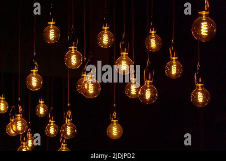 Many vintage light bulbs hanging on cords and glowing against black background at night Stock Photo