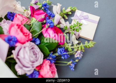 Close up of summer bouquet of roses foxgloves bachelor buttons flowers wrapped in paper and arranged on background with gift box. Fresh blooms for hol Stock Photo