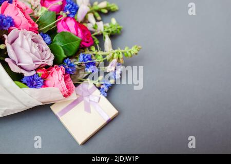 Close up of summer bouquet of roses foxgloves bachelor buttons flowers wrapped in paper and arranged on background with gift box. Holiday present Stock Photo