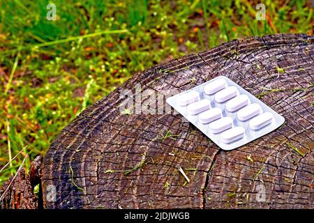 White pills in blister on green grass with stump. Stock Photo