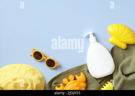 Baby sun tan cream, sunglasses, sand molds and panama hat on blue table. Kids sun protection concept. Stock Photo
