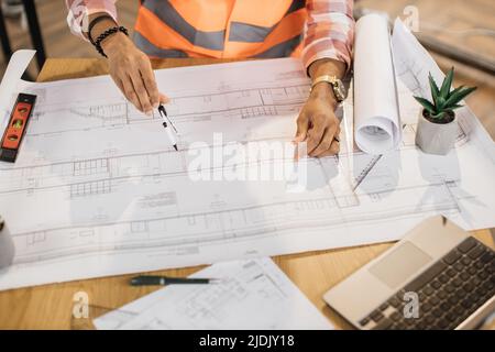 Close up of hands of african builder drawing renovation house equipment architects on the desk with a blueprint using compass, ruler and pen in the office. Concept of architects, construction, design. Stock Photo