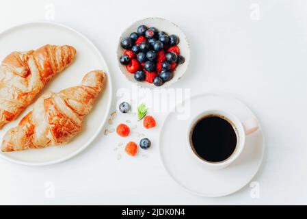 Coffee, croissants and berries breakfast on a white table. Top view, flat lay.