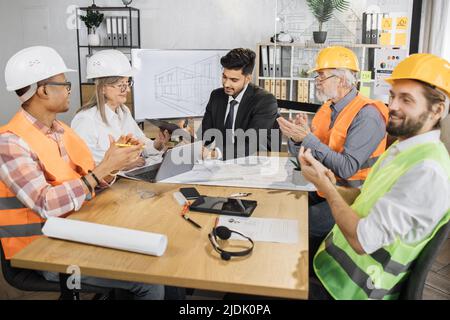Business people working on common building project. Indian businessman signs contract and documents of senior woman boss of a construction company while employees clapping their hands. Stock Photo