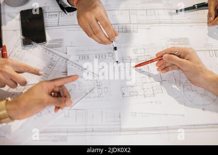 Close up of architects, engineers and designers sitting together at table and analysing blueprints. People of different ages and races working at office. Creation of construction project. Stock Photo
