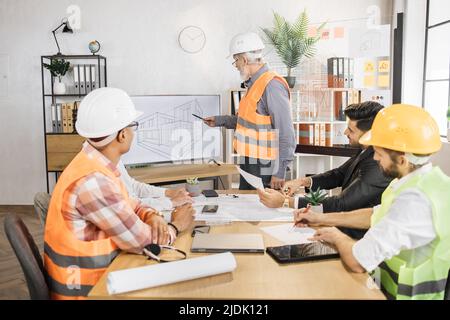 Group of five international partners having working meeting to discuss design and measurements of new building looking on interactive digital screen with house drawing. Teamwork, brainstorming concept Stock Photo