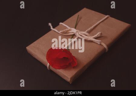 gift is wrapped in craft paper on top lies a bouquet of red poppies on a dark background Stock Photo