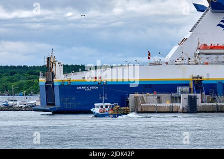 Lobster boat loaded with fresh lobsters returns to port in North Sydney Cape Breton Nova Scotia.  The fishing boat is dwarfed by the Nova Scotia to Ne Stock Photo