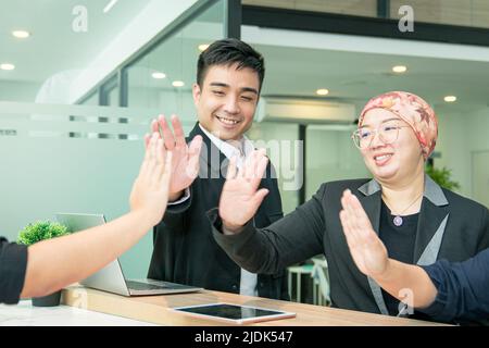 Happy business co workers giving high to one another in office. Symbol of unity, teamwork or victory. Stock Photo