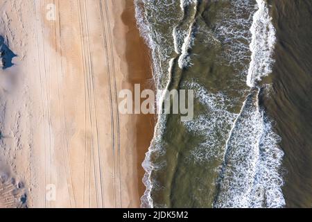 Aerial view of waves breaking with tire tracks in the sand Stock Photo