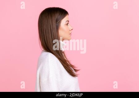 Side view portrait of serious female looks ahead with strict expression, expressing negative emotions, wearing white casual style sweater. Indoor studio shot isolated on pink background. Stock Photo