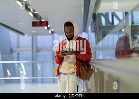 African man with smartphone in airport terminal, young black guy traveler waiting for plane boarding Stock Photo