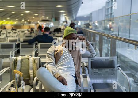Happy young black man sitting in airport terminal resting waiting landing on board looking at window Stock Photo
