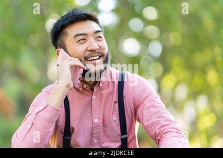 Smiling asian man talking to the mobile in a park Stock Photo