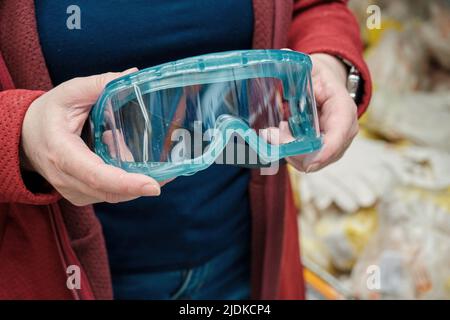 Woman in building materials store chooses for buy protective glasses of plastic Stock Photo
