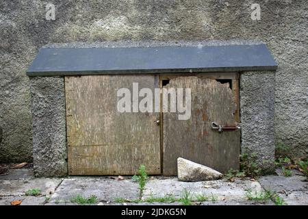 two low wooden doors in a cement cupboard with sloping roof and a grey wall behind Stock Photo