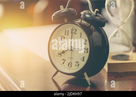8 o'clock time retro clock with sand hourglass on wood table with sun light background Stock Photo