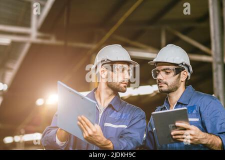 Team Industry Engineers worker in metal Factory using Digital Tablet Computer talking discussion help together. Stock Photo