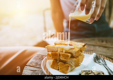 people pouring sweetened condensed milk on top of buttered toast enjoy eating fat and sweet menu in cafe. Stock Photo