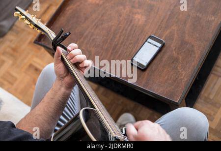 Amateur guitarist reading chords on mobile phone. Selective focus Stock Photo