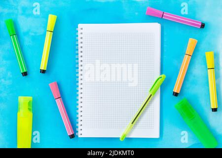 Checkered notebook with pen and multi-colored markers and felt-tip pens on blue watercolor background. Back to school concept, drawing. Copy space Stock Photo