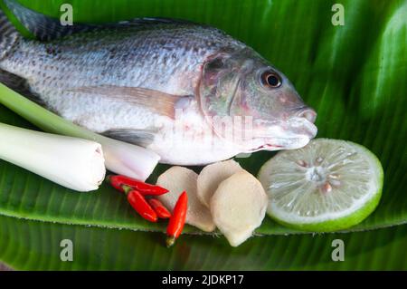 To view of fresh tilapia fish with lemongrass, lemon and chili on banana leaf. Asian food concept Stock Photo