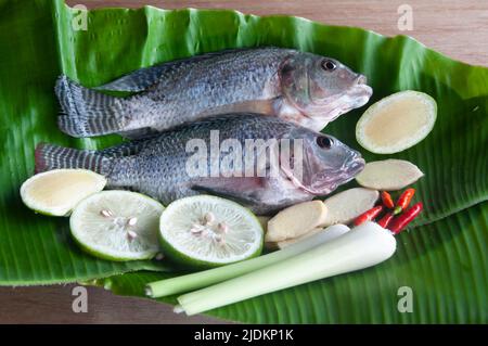 Fresh tilapia fish with lemongrass, lemon and chili on banana leaf. Stock Photo