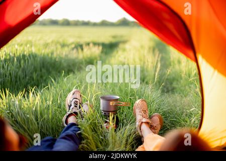 Couple sit in tent and prepare food, close-up on shoes Stock Photo