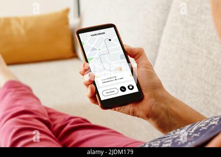 Woman on the sofa checking an online order status with delivery tracking app on smartphone. Stock Photo