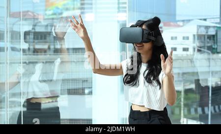 Excited female employee wearing virtual reality glasses, interacting with digital interface at modern office. Innovation concept Stock Photo