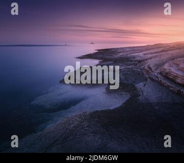 Rocky sea coast and lighthouse at colorful sunset in summer Stock Photo