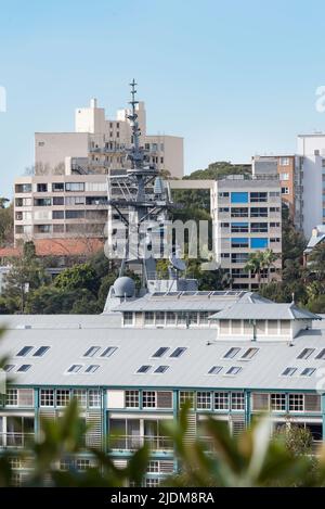 The mast of an Australian Navy, Hobart Class air warfare destroyer rises over the roof of the hotel and Finger Wharf in Woolloomooloo Bay, Sydney Stock Photo