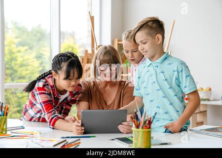 Mature teacher and pupils using tablet computer during class in art school indoors Stock Photo