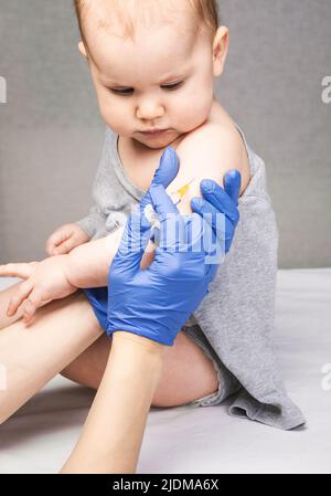 Pediatrician or nurse giving an intramuscular injection of a vaccine to arm of a baby girl during coronavirus COVID-19 pandemic Stock Photo