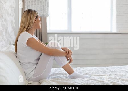 Depressed blonde lady sitting on bed at home Stock Photo
