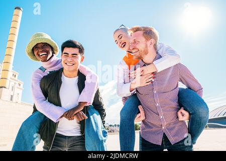 outdoors photo of happy boyfriends piggybacking their girlfriends. Group Of Friends Having Fun Together. Cheerful young loving couples friends walking Stock Photo