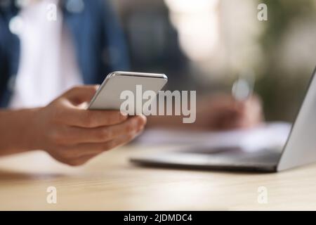 Young Male Using Modern Smartphone While Sitting At Desk With Laptop Stock Photo