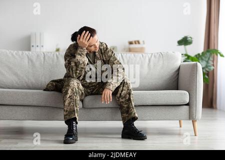 Mental Disorders In Military. Depressed Soldier Lady In Uniform Sitting On Couch Stock Photo