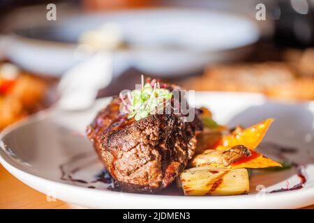 Cooked grilled beef meat with mushrooms and vegetables on white plate in luxury restaurant. Freshly roasted steak ready to eat. Sun light. Fine dining Stock Photo