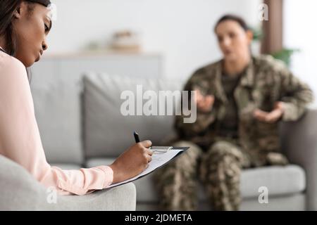 Black Female Psychologist Taking Notes During Therapy Session With Military Woman Stock Photo