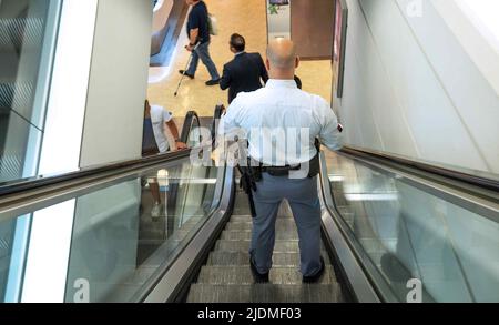 Masculine security guard standing, on escalator in department store. Stock Photo