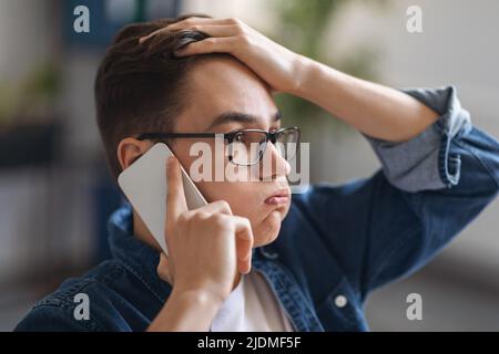 Worried Young Man Talking On Cellphone And Touching Head In Stress Stock Photo
