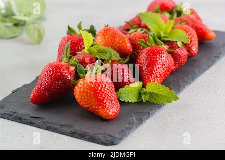 Large red ripe strawberries and mint petals lie on a stone slate dish. Selective focus Stock Photo