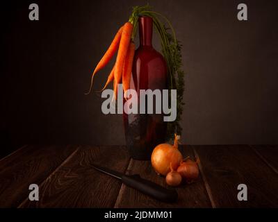 Still life of organic carrots resting on a vase, onions and a knife on a dark wood table with a dark background tor copy Stock Photo